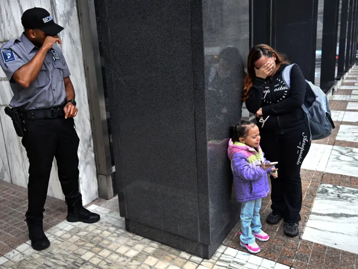 A security guard at a federal building puts his hand over his face crying around the corner from a woman and child also crying after their loved one was detained by Immigration and Customs Enforcement.