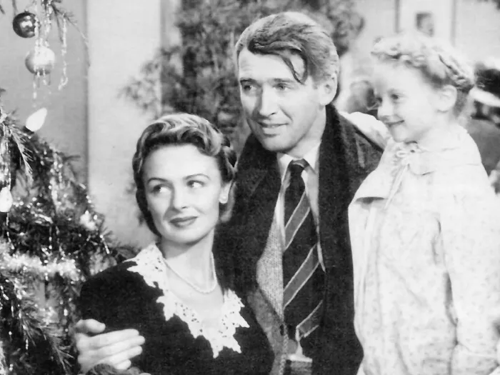 In a movie still from "It's a Wonderful Life" a woman and man, who is holding a young girl in his arm, look at a Christmas tree.