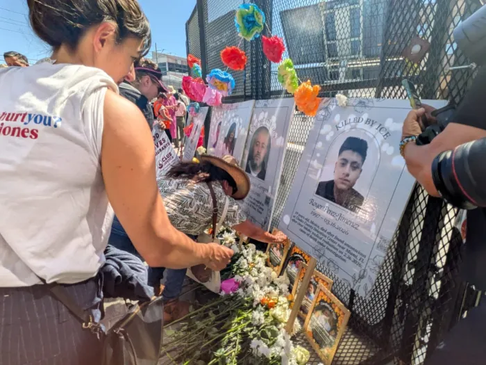 People gather around a memorial with flowers and crosses.