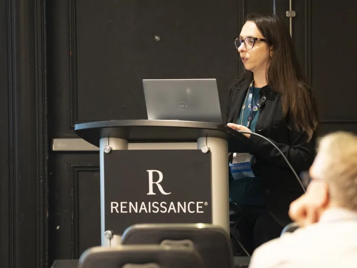 A young woman speaks at a hotel lectern with her laptop computer open