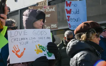 Woman stands in a crowd holding a sign supporting immigrants
