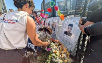 People gather around a memorial with flowers and crosses.